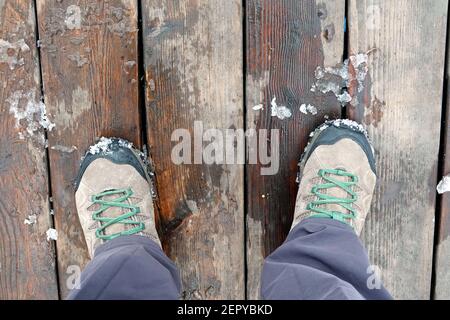 Les pieds du touriste se sont mis en paire de chaussures de randonnée sport les vieilles planches en bois brun sont en plein air le jour du printemps vue du dessus en gros plan Banque D'Images