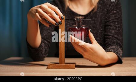 La sorcière prépare une potion. Potion d'amour rouge dans un pot en verre en forme de cœur. Concept magique d'amour Banque D'Images