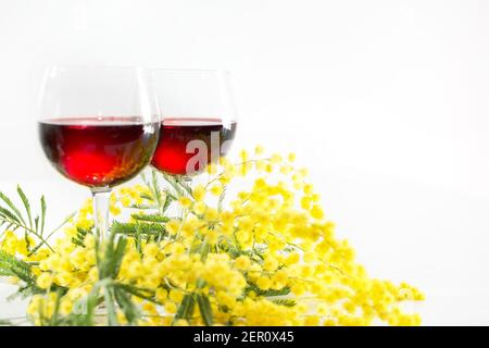 branche de mimosa et deux verres de vin rouge un arrière-plan blanc Banque D'Images