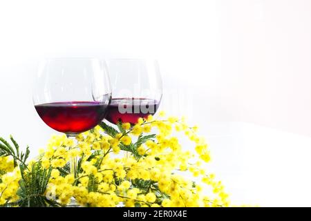 branche de mimosa et deux verres de vin rouge un arrière-plan blanc Banque D'Images