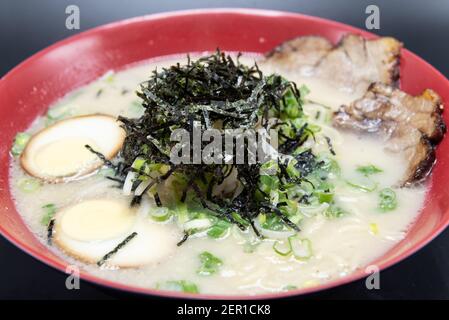 Grand bol de Tonkotsu Ramen épicé servi avec une pile d'algues sur le dessus avec du porc braisé et des demi-œufs durs. Banque D'Images