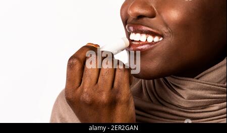 Femme noire appliquant un baume hygiénique pour les lèvres sur fond clair Banque D'Images