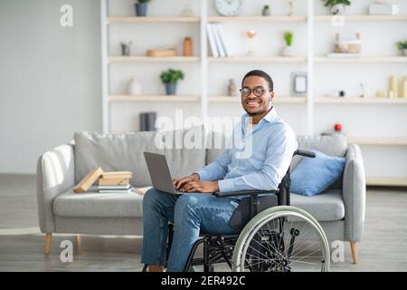 Homme noir handicapé heureux en fauteuil roulant utilisant un ordinateur portable, travaillant en ligne de la maison, espace de copie Banque D'Images