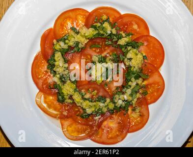 Gros plan du carpaccio de tomate finement émincé avec une vinaigrette aux herbes, aux oignons de printemps et au gingembre sur une assiette blanche Banque D'Images