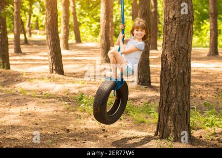 Petite fille mignonne balançant sur la roue attachée au grand arbre dans la forêt d'automne.