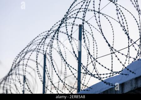 Une clôture barbelée à pointe effilée en fil de rasoir enroulée sur le dessus du le mur protège des prisonniers et des criminels en prison et de entrée dans la zone restreinte ou Banque D'Images