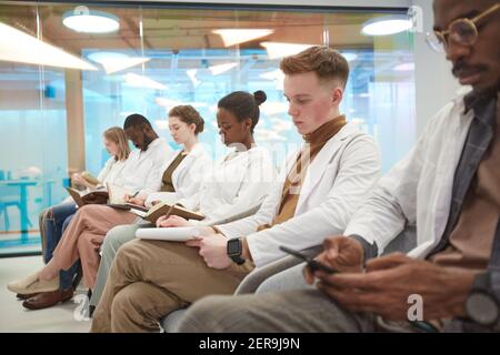 Groupe multiethnique de personnes portant un blouse de laboratoire assis dans la rangée et prenant des notes pendant la conférence sur la médecine à l'université, salle de copie Banque D'Images