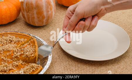 Tarte à la citrouille maison fraîchement cuite décorée de noix écrasées et de zeste d'orange. Femme mains servant la tarte sur une assiette, vue rapprochée Banque D'Images