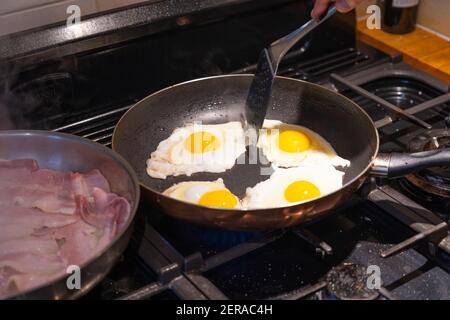 Les œufs frits dans une poêle et séparés par une spatule, cuits sur une table de cuisson à gaz pour un petit déjeuner anglais traditionnel Banque D'Images