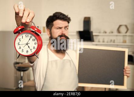 Appelez pour la livraison. Heure du repas. Nourriture et boissons saines. Femme de ménage dans la cuisine. Cuisine par recette. Menu hippster barbu. Foyer sélectif. Espace de copie. Homme avec planche et réveil. Banque D'Images