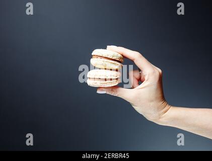 La main femelle tenant des macarons français colorés. Délicieux dessert sur fond gris foncé Banque D'Images