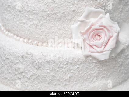 Gâteau blanc à deux niveaux avec copeaux de noix de coco décoré avec fleur de rose gros plan. Banque D'Images