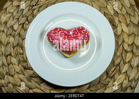 Un donut en forme de coeur rempli de pâte à gâteau, trempé dans le glaçage rouge, et recouvert de saupoudrés de Saint-Valentin festifs Banque D'Images