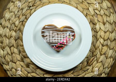 Un donut en forme de coeur rempli de pâte à gâteau, trempé dans le glaçage rouge, et recouvert de saupoudrés de Saint-Valentin festifs Banque D'Images