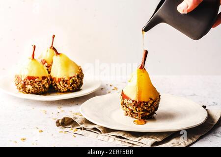 Couvre-poire pochée au chocolat et au granola maison, sur une assiette avec du sirop égoutté sur le dessus. Banque D'Images