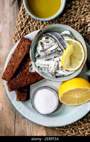 Bol d'anchois marinés ou filet de sardines dans l'huile, servi avec du citron, de l'huile d'olive, du sel et du pain de seigle grillé pour des tapas ou des antipasti sur le vieux bois b Banque D'Images