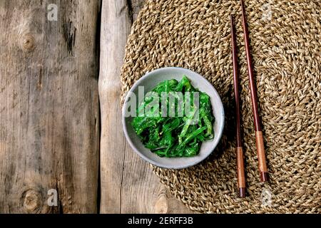 Salade japonaise d'algues Wakame chuka aux graines de sésame dans une plaque en céramique avec baguettes sur fond de bois ancien. Flat lay, espace de copie Banque D'Images