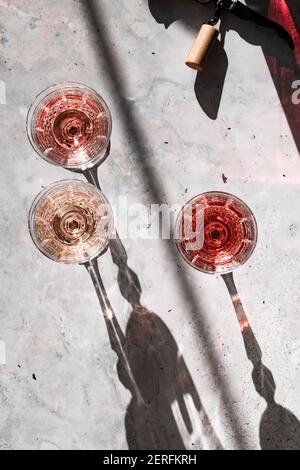 Trois nuances de vin de Rose dans des verres jetant des ombres dures entourées d'ombres colorées projetées à partir des bouteilles de vin. Banque D'Images