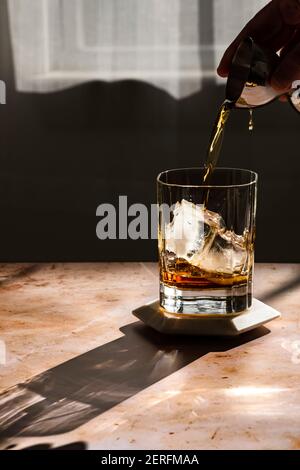 Le whisky est versé dans un verre rocailleux en lumière dure. Banque D'Images