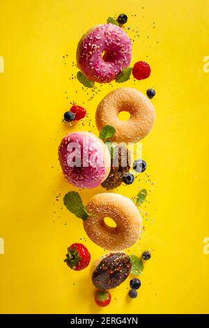 Décorées avec divers beignets sprinkles et de baies dans motion relevant sur yelloy arrière-plan. Beignets sucrés et colorés de tomber ou voler dans moti Banque D'Images