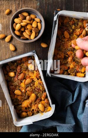 Une main de femme plaçant des amandes sur un mélange de gâteau de fruits dans un moule à pain. Banque D'Images