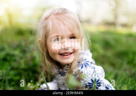 Petite fille souriante avec fleurs de printemps sur pelouse verte dans le jardin. Photo de haute qualité Banque D'Images