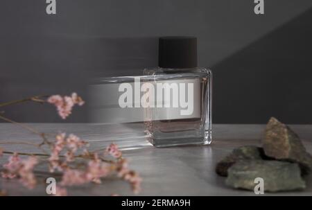 Bouteille de parfum avec fleurs roses sur fond gris foncé. Étiquette blanche isolée. Copier l'espace Banque D'Images