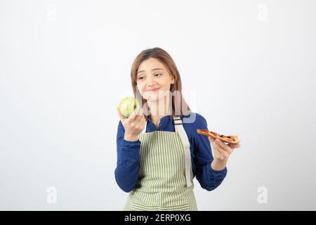 Image de la femme en tablier essayant de choisir quoi mangez de la pomme ou de la pizza Banque D'Images