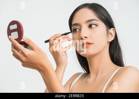 race mixte asiatique femme mettant le traceur d'oeil sur la paupière arrière-plan blanc Banque D'Images