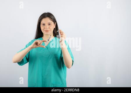 Femme médecin portant une seringue de maintien uniforme verte sur fond blanc Banque D'Images