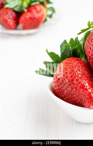 Vue de dessus des fraises dans un bol blanc et assiette avec plus de fraises, mise au point sélective, sur table blanche, à la verticale Banque D'Images