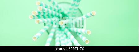 pile de papier pailles à boire blanches et vertes rayées pour faire la fête dans une tasse en verre transparent sur fond vert. bannière Banque D'Images