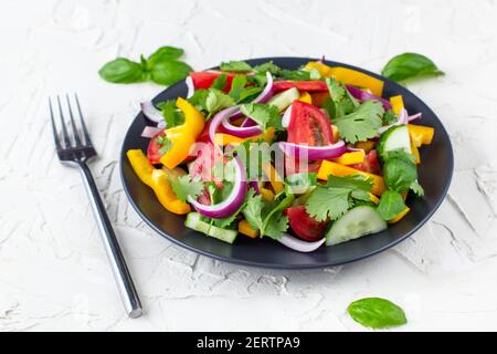 Assiette de salade arc-en-ciel avec différents légumes et herbes plaque noire avec fourche sur fond de pierre blanche Banque D'Images