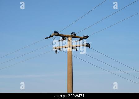 Poteau électrique en béton avec isolants en céramique et lignes de tension, en fond bleu ciel avec ciel bleu. Banque D'Images