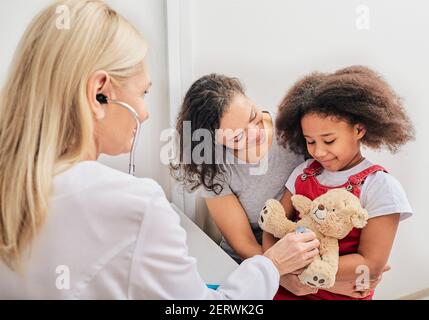 Le pédiatre tient un stéthoscope, communique avec une petite patiente. Médecin enfant en visite avec mère, santé des enfants Banque D'Images