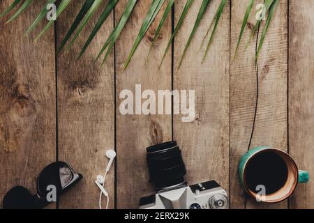 Flat Lay Travel concept, appareil photo, tasse de café, lunettes et écouteurs, feuille de palmier sur fond de bois. Photo de haute qualité Banque D'Images