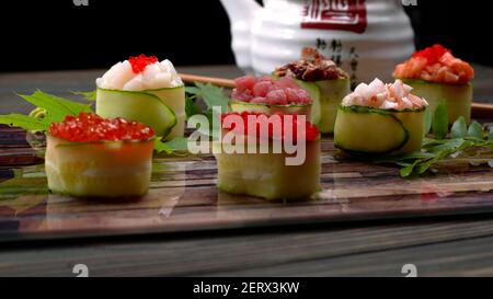 Gunkan maki dans un concombre, avec caviar, thon, pétoncle, anguille, crevettes, anguille et saumon, sur une planche en bois, avec des feuilles d'érable et d'acacia, à faible profondeur Banque D'Images