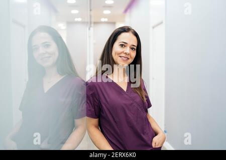 Photo de la femme heureuse portant un uniforme regardant l'appareil photo et souriant. Elle travaille dans une clinique dentaire. Banque D'Images