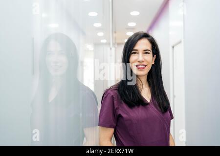 Photo de la femme heureuse portant un uniforme regardant l'appareil photo et souriant. Elle travaille dans une clinique dentaire. Banque D'Images