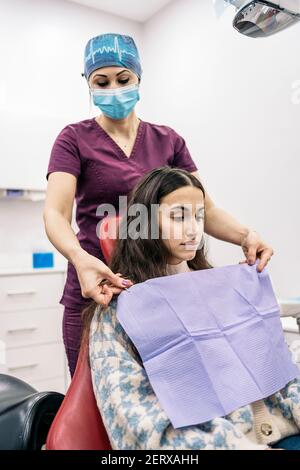 Photo de stock de femme dentiste portant un masque facial préparant la fille pour son check-up. Banque D'Images