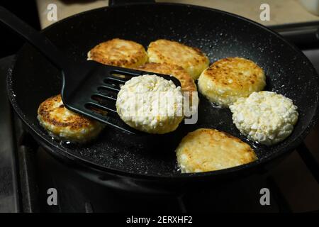 Les crêpes au fromage cottage sont frites pour le petit déjeuner dans une poêle noire en gros plan. Retourner les crêpes au fromage cottage à l'aide d'une spatule Banque D'Images