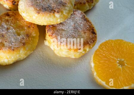 Délicieuses crêpes au fromage cottage avec du sucre en poudre, avec une orange sur une assiette blanche en gros plan Banque D'Images