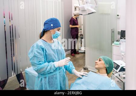 Photo de la femme dentiste portant un masque de visage discutant avec sa jeune patiente dans la clinique dentaire. Banque D'Images