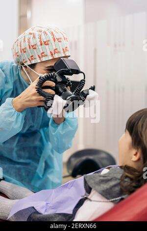 Photo d'une femme dentiste portant un masque facial prenant en photo un jeune patient. Banque D'Images