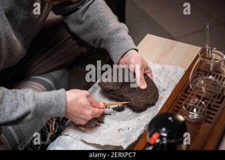 Prise de vue sans visage. Gros plan des mains du maître en train de cueillir un gâteau à thé avec une aiguille pour une cérémonie du thé ou une dégustation de thé chinois. Banque D'Images