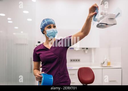 Photo de la femme dentiste travaillant dans une clinique dentaire moderne et portant un masque facial. Banque D'Images