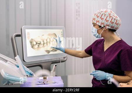 Photo de la femme employée d'une clinique dentaire montrant une radiographie à un patient. Banque D'Images