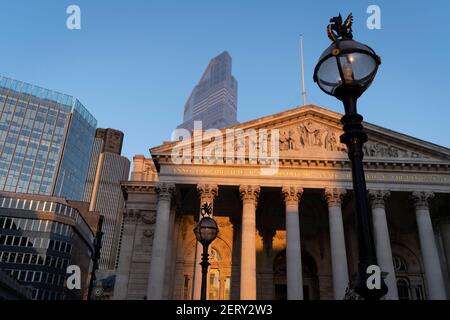 Avec des bureaux modernes d'institutions financières derrière, une vue panoramique architecturale sur les frises et inscriptions latines sur le fronton de la Bourse royale dans la ville de Londres, le quartier financier de la capitale, le 27 février 2021, à Londres, en Angleterre. Au sommet des colonnes doriques et ioniques avec leur travail en pierre, des linteaux puissants se croisent, portant la charge de l'art et des sculptures fines qui présentent le design de Sir William Tite en 1842-1844 et ouvert en 1844 par la reine Victoria dont le nom est écrit en latin (victoriae R). C’est le troisième bâtiment du genre érigé sur la sa Banque D'Images