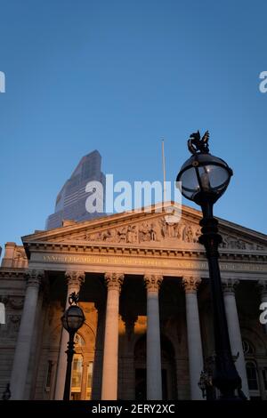 Avec des bureaux modernes d'institutions financières derrière, une vue panoramique architecturale sur les frises et inscriptions latines sur le fronton de la Bourse royale dans la ville de Londres, le quartier financier de la capitale, le 27 février 2021, à Londres, en Angleterre. Au sommet des colonnes doriques et ioniques avec leur travail en pierre, des linteaux puissants se croisent, portant la charge de l'art et des sculptures fines qui présentent le design de Sir William Tite en 1842-1844 et ouvert en 1844 par la reine Victoria dont le nom est écrit en latin (victoriae R). C’est le troisième bâtiment du genre érigé sur la sa Banque D'Images