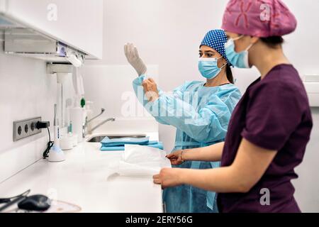 Photo de stock des femmes portant un masque facial et un filet de cheveux travaillant dans une clinique dentaire moderne. Banque D'Images